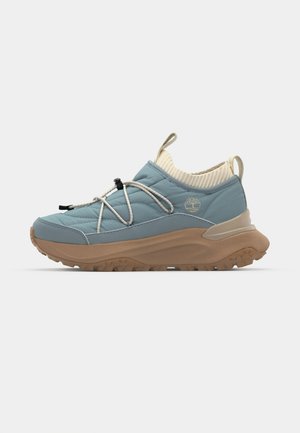 Quota met een blauwe quilted sneaker met een dikke beige zool, elastische bungee veters, geribbeld textuur op de zool en een geribbelde crèmekleurige kraag.