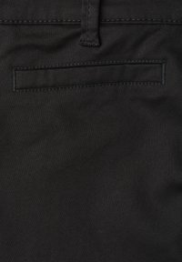 Poche arrière d’un pantalon noir avec une poche passepoilée horizontale et une boucle de ceinture visible au-dessus de la couture.