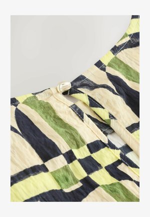 Löysä pusero, jossa on monivärinen ruutukuosi vihreänä, keltaisena ja laivastonsinisenä. Puserossa on avainreikäaukko ja koristeellinen napin suljenta.