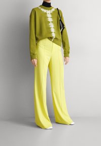 Zielona bluzka z długim rękawem w wzór tie-dye, połączona z jasnobordowymi spodniami o szerokich nogawkach. Czarne golf pod spodem i mała czarna torebka.