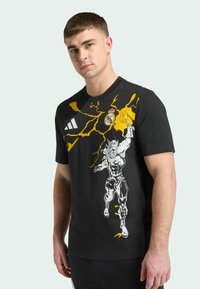 Czarny bawełniany t-shirt z postacią w stylu komiksowym w białych i żółtych akcentach. Logo Adidas na piersi z herbem Realu Madryt.