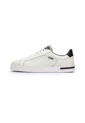 Zapatillas de cuero blanco con una textura suave, acento negro en el talón y perforaciones laterales. Presentan una suela de goma blanca con detalles en negro.