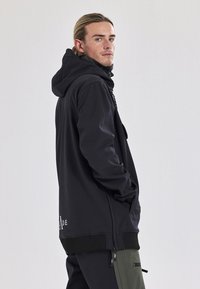 Zwart lange mouwen hoodie met een trekkoordkap, voorzien van een ritssluiting voorzak, zijsplitten en een geribbelde onderrand. Het materiaal lijkt glad.