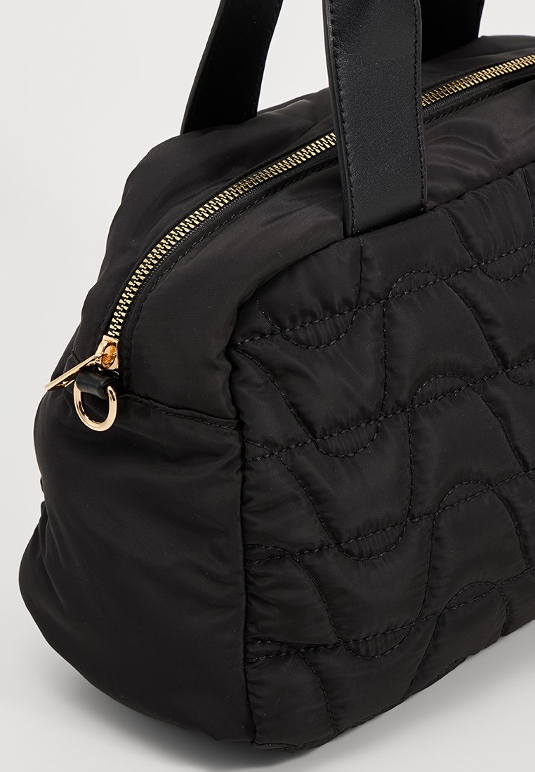 Czarna pikowana torebka o zaokrąglonym kształcie, z złotym zamkiem błyskawicznym i skórzaną rączką. Miękki materiał o gładkiej teksturze i subtelnym przeszyciu.