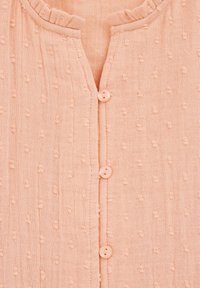 Close-up breskve tkanine z teksturiranimi pikami in tremi usklajenimi gumbi vzdolž osrednjega šiva.