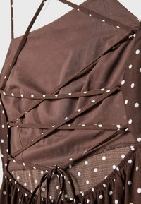 Robe marron à pois blancs avec un détail à lacets au dos noué en un nœud, mettant en valeur la texture du tissu et les coutures.