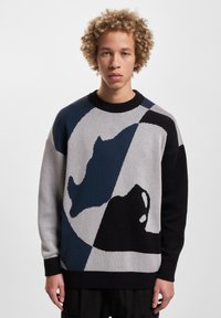 Knit sweater featuring block colors of black, gray, navy, and white, with abstract patterns and a ribbed crew neckline and cuffs.