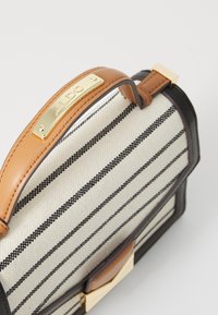 Sac en toile rayé avec des accents en cuir marron et une plaque de logo dorée. Dispose d'une forme structurée et d'une poignée supérieure.