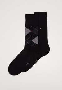 Schwarze Baumwollsocken mit einem Argyle-Muster in Grautönen und Weiß, mit einem kleinen roten Akzent und einem Logo am Knöchel.