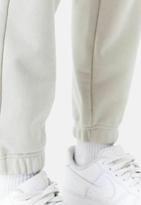 Hellgraue tapering Sweatpants mit elastischen Bündchen, kombiniert mit weißen Sneakers. Der Stoff wirkt weich und strukturiert und zeigt einen lässigen Look.
