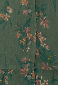 Tissu vert à motif floral avec des fleurs roses et jaunes, doté de boutons ronds et d'une surface légèrement texturée.