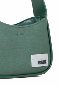 Sacoche verte en tissu texturé avec une bandoulière lisse semblable au cuir. Présente un logo et une étiquette embossés aux couleurs contrastées.