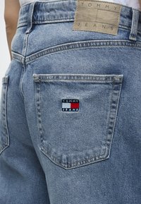 Ανοιχτό μπλε τζιν από denim σε άτομο, με το λογότυπο Tommy Jeans στο πίσω τσεπάκι και δερμάτινη ετικέτα με την επωνυμία στη μέση.