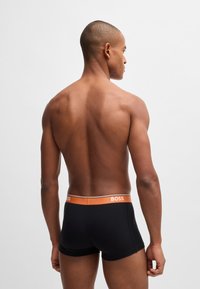 Boxer-briefs noirs avec une taille orange arborant la marque 'BOSS'. Tissu doux et extensible avec un ajustement serré et une texture lisse.