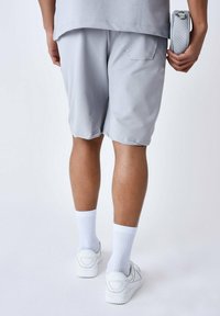 Shorts de sport gris en tissu doux, avec une taille élastique et une poche latérale. Associés à des chaussettes blanches et à des baskets blanches.