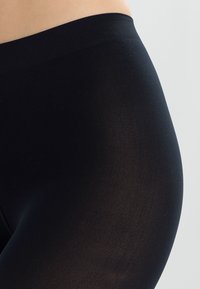 Čierne legíny vyrobené z elastickej, textúrovanej tkaniny. Vysoký pás s hladkými okrajmi, priliehavý strih a žiadne viditeľné švy.