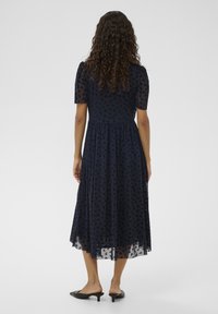 Tengerészkék midi ruha áttetsző rövid ujjal, virágmintával, testhezálló felsőrésszel és légies szoknyával. Cipzáras, enyhén áttetsző szegéllyel.