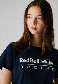 T-shirt in cotone blu navy con logo "Red Bull RACING" in bianco. Maniche corte, collo tondo e texture liscia.