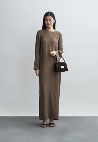 Robe marron à manches longues, coupe droite et tissu texturé. Associée à un sac à main en daim marron foncé avec une petite fermeture métallique.