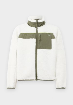 Veste en polaire blanche avec des accents olive, col montant, poche poitrine zippée et poignets côtelés. Présente un logo sur le côté gauche.