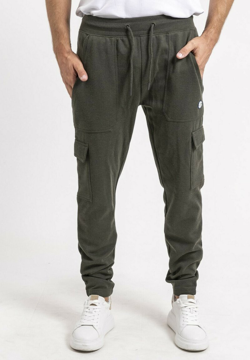 Pantalons de jogging kaki en tissu texturé, avec une taille élastique, des cordons de serrage ajustables, des poches latérales et des chevilles fuselées, associés à des baskets blanches.