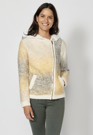 Veste à capuche en tricot texturé avec un mélange de jaune, gris et crème. Dotée d'une fermeture éclair à l'avant, de poches latérales et de poignets côtelés.