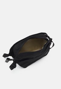 Bolso negro con cierre de cremallera, con un interior beige. El exterior tiene correas ajustables y una textura suave.
