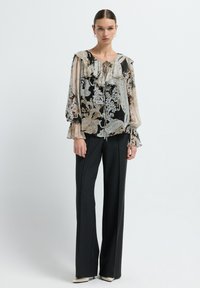 Blusa fluida con motivo floreale in crema e nero, colletto volant, abbinata a pantaloni a gamba larga a righe nere e scarpe bianche con punta.