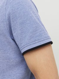 Blauw polo-shirt van textuurstof, met een zwart-wit gestreepte bies op de mouw. Close-up van de arm en mouwdetail.