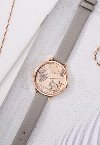 Reloj de oro rosa con correa de cuero gris claro. Presenta una escena de vida salvaje con una ardilla, hojas y detalles brillantes en la esfera.