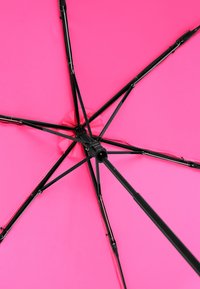 Parapluie rose avec une toile en tissu lisse, un cadre en métal noir et un moyeu central. Il présente plusieurs nervures de support noires.