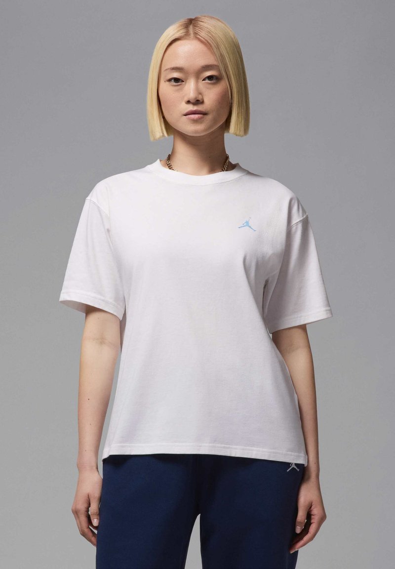 Camiseta de algodón blanca con un corte relajado, que presenta un logotipo de Jordan en color azul claro en el lado izquierdo del pecho. Mangas cortas y cuello redondo.