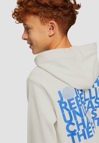 Lichtgrijze hoodie met een groot blauw grafisch tekst op de achterkant, versierd met cirkelvormige elementen. Zachte stof met een ontspannen pasvorm en een capuchon.