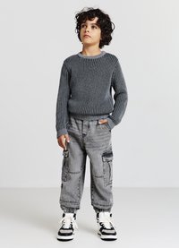 Maglione grigio a coste, pantaloni cargo grigi con tasche e sneaker bianche e nere. L'outfit presenta una vestibilità comoda e polsini elasticizzati.