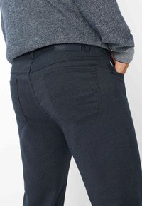 Donkerblauwe denim jeans met een gestructureerd oppervlak, slim fit ontwerp en subtiele stiksels. Achterzak zichtbaar.