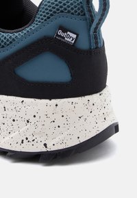 Κοντινό πλάνο της φτέρνας ενός αδιάβροχου παπουτσιού μπλε και μαύρου χρώματος με λευκή σόλα με στίγματα και ετικέτα "OutDry".