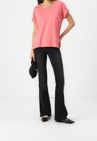 Haut rose à manches courtes, coupe décontractée. Associé à un jean noir évasé et des ballerines noires pointues ornées de ferrures décoratives. Tenue d'un sac noir.