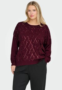 Burgundowy sweter z wzorami w diamenty. Długie rękawy i okrągły dekolt. Materiał wygląda na dzianinowy o miękkiej teksturze.