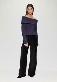 Lila, schulterfreie Strickpullover mit geripptem Muster, kombiniert mit schwarzen Samt-Hosen im weiten Schnitt und schwarzen Slippern.