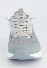 Chaussure de sport grise avec un upper en mesh, des détails texturés, des lacets plats et une semelle en caoutchouc blanche. Design minimaliste avec un bout arrondi.