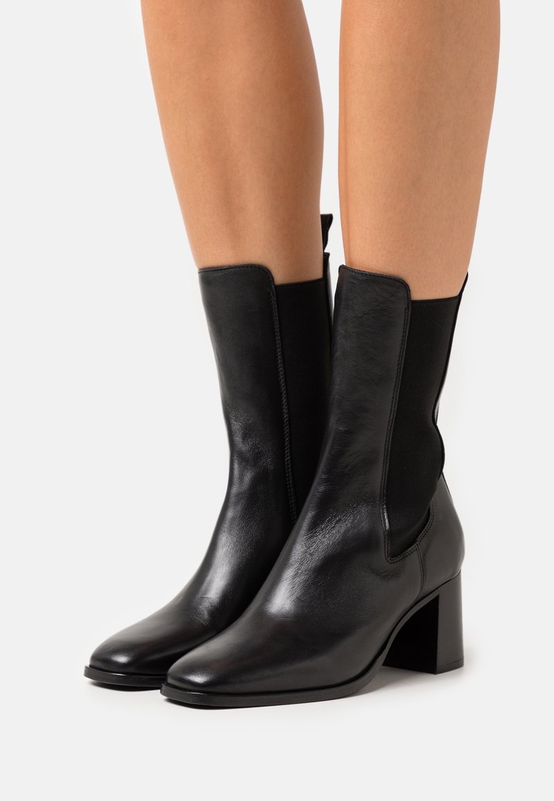 Bottes basses en cuir noir à finition lisse, avec des panneaux latéraux élastiques et un design à bout carré sur un talon bloc.