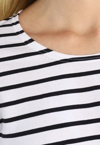 Sort og hvid stribet bomulds T-shirt med rund halsudskæring og korte ærmer, der har en glat tekstur og et jævnt mønster.