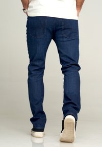 Mörkblå denimjeans med smal passform. Har två bakfickor och subtila sömmar. Bärs med svartvita sneakers.