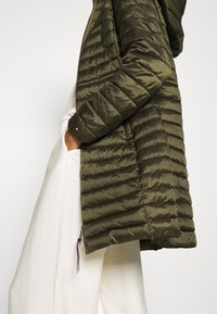 Giacca trapuntata verde oliva con cappuccio, tasche con zip e polsini elasticizzati. Tessuto morbido e lucido.