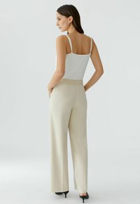 White spaghetti strap top paired with cream wide-leg pants. Smooth fabric with a tailored waistband and back pockets. Black heels accent the outfit.