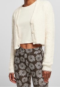 Vit, fluffig cardigan med en croppad design, med knäppning framtill och långa ärmar, lagd över en krämfärgad topp och blommönstrade leggings.