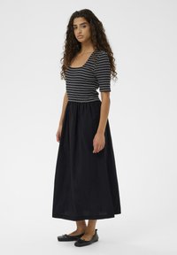 Črtasta črno-bela oprijeta majica s kratkimi rokavi, kombinirana s pretočno črno maksi krilo, dopolnjena s črnimi ravnimi čevlji.