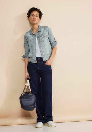 Light blue denim jacket with two chest pockets, white T-shirt, dark blue wide-leg jeans, and a round navy handbag. White sneakers on feet.