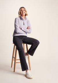 Light purple fleece pullover with a half-zip collar, paired with black straight-leg jeans and white sneakers, sitting on a wooden stool.