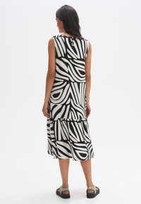 Sleeveless dress in black and white abstract pattern, tiered design, made of lightweight fabric, features a back button closure.